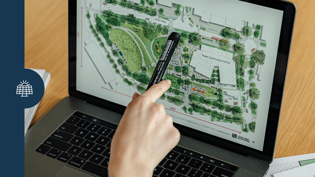 Regional energy coach program person working at computer pointing at the plan of a site